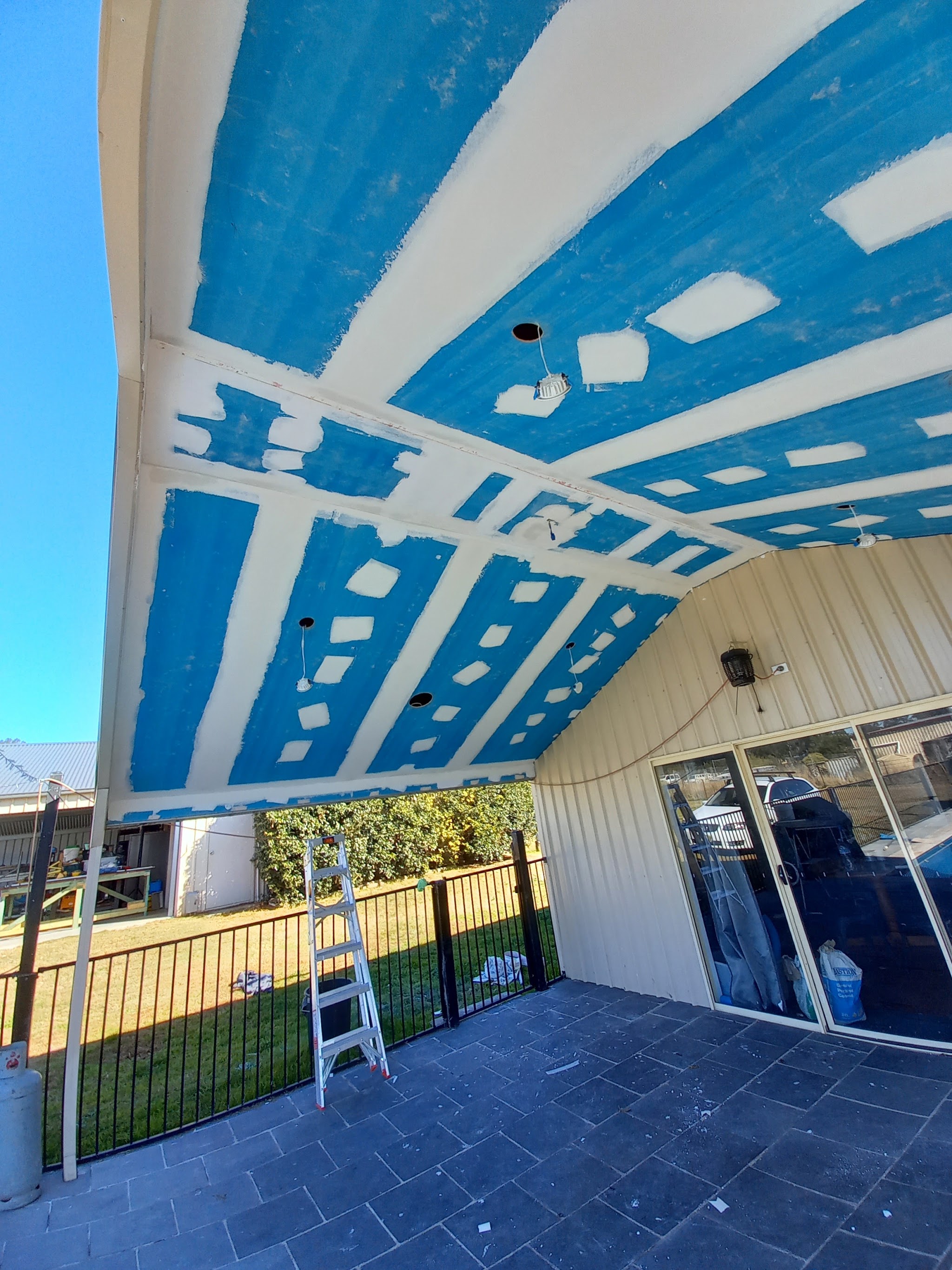 An outdoor alfresco ceiling sheeted in blue wet area board with every joint set, under a clear sky