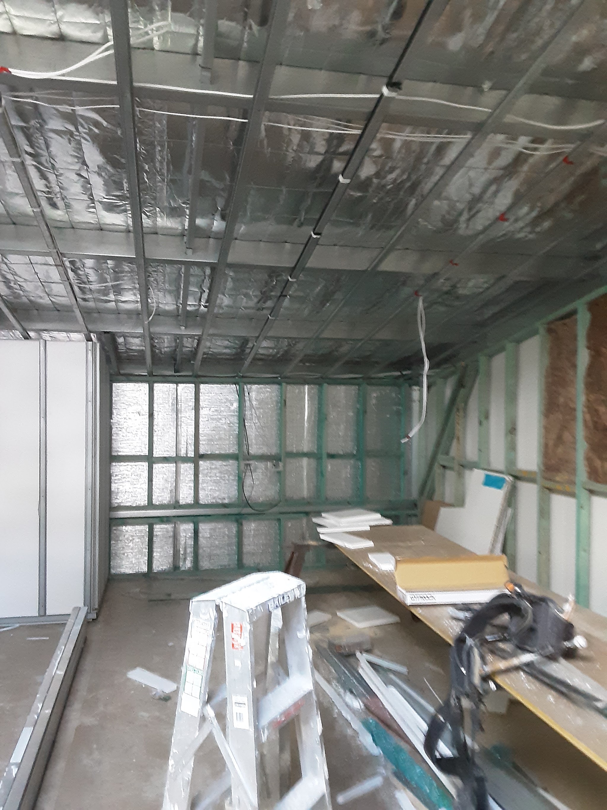 A suspended steel ceiling frame with foil sarking and insulation, sheets stacked ready to hang