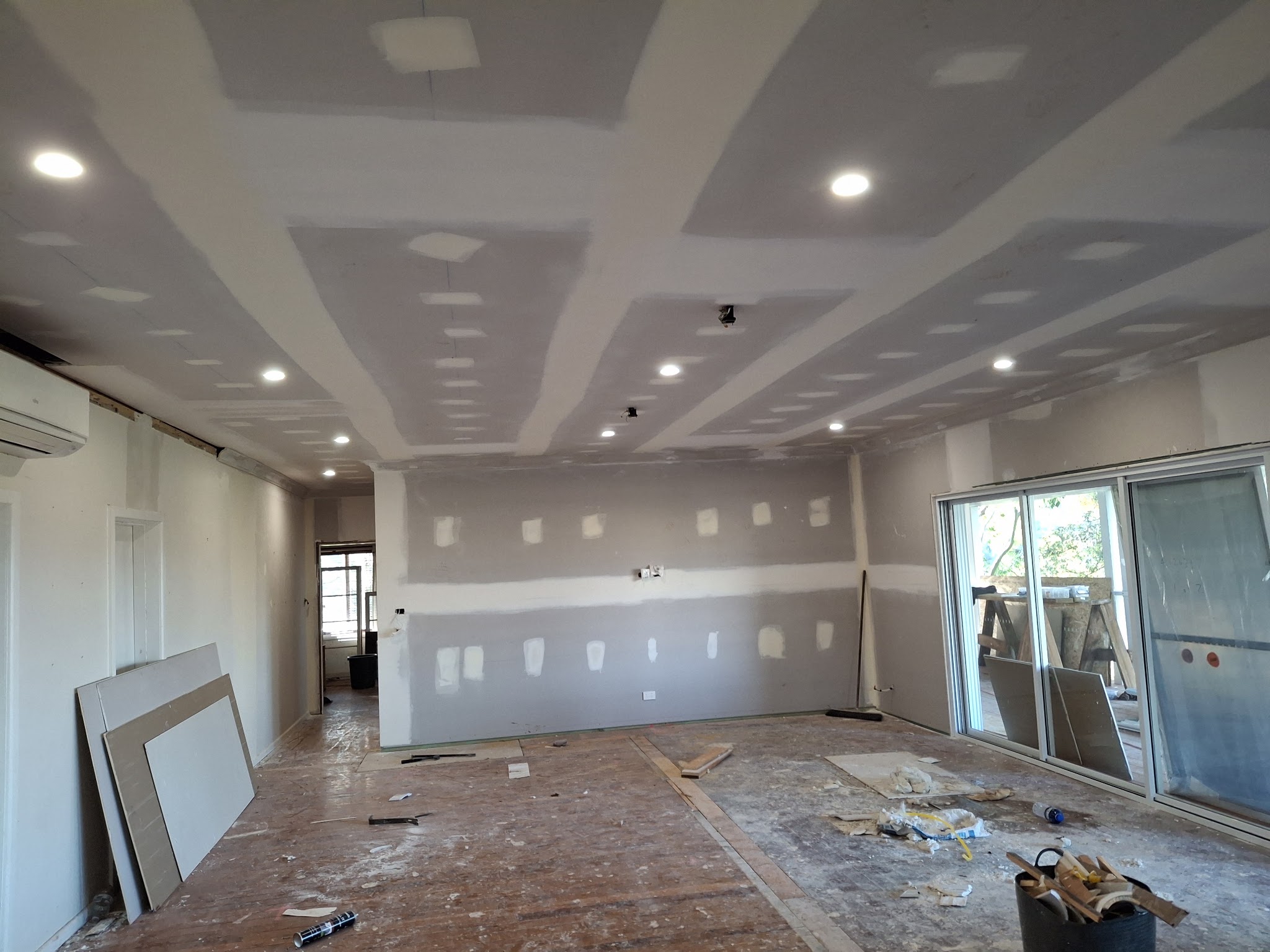 A large open plan living area with stepped ceiling bulkheads set and sanded and the downlights already fitted